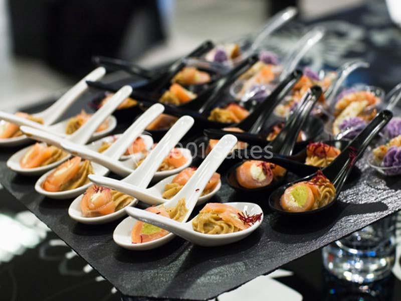 Cuillères apéritives variées disposées sur un plateau, contenant saumon, mousse et autres garnitures colorées.