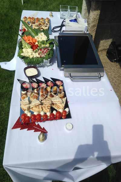 Table avec nappes blanches présentant des plateaux de bouchées apéritives, légumes, et sauces, en extérieur.