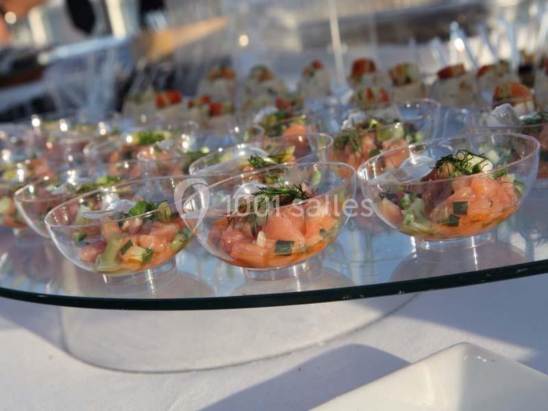 Coupes transparentes contenant des portions de tartare de saumon avec herbes fraîches, présentées sur un plateau en verre.