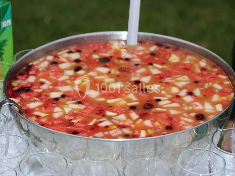 Bol de punch aux fruits avec morceaux de pastèque, pomme et baies, entouré de verres transparents.