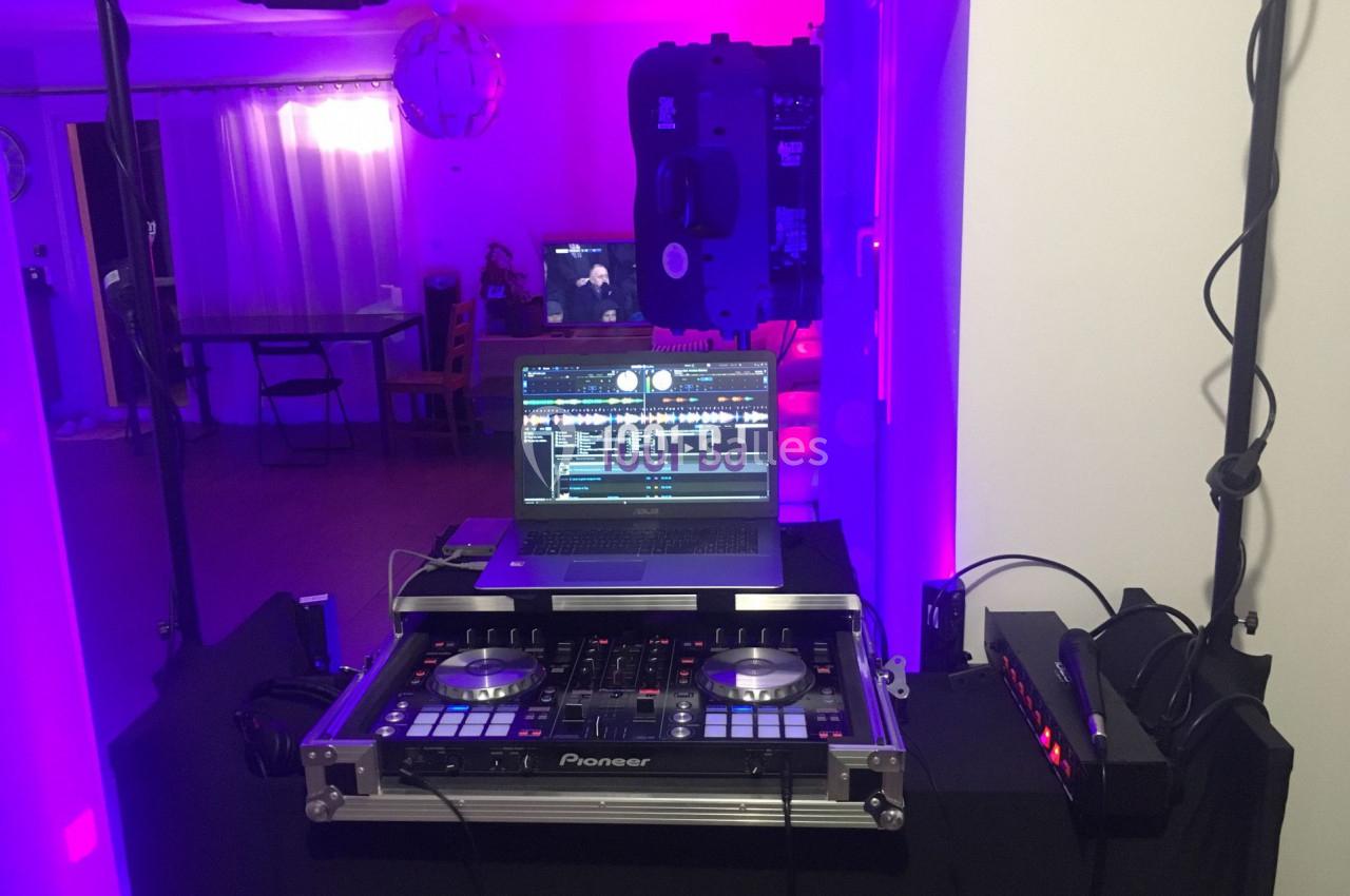 Poste de DJ avec une console Pioneer et un ordinateur portable, installé dans une pièce éclairée par des lumières violettes.