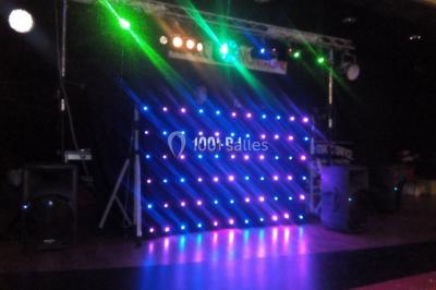 Un DJ mixe derrière une table éclairée de lumières LED violettes, avec un mur décoratif en arrière-plan.