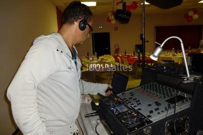 Un DJ mixe derrière une table éclairée de lumières LED violettes, avec un mur décoratif en arrière-plan.