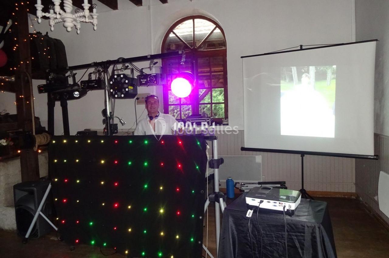 Un DJ anime une soirée avec un équipement lumineux et un projecteur affichant une image sur un écran.