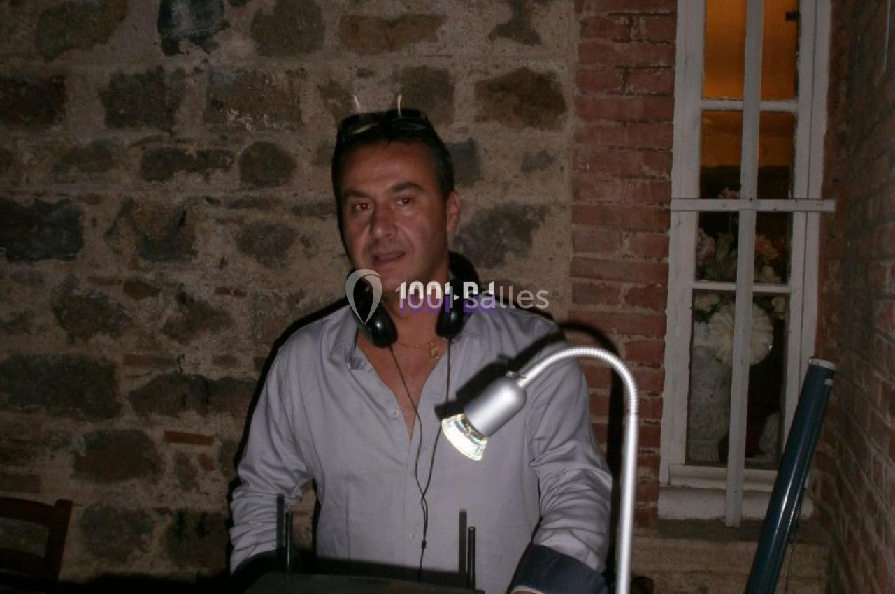 Homme debout derrière une table de mixage dans une pièce aux murs en pierre, éclairée par une lampe.