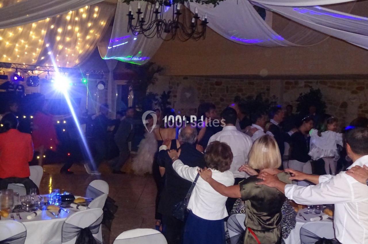 Des invités dansent en cercle sous un plafond décoré de drapés et de lumières dans une salle de réception.