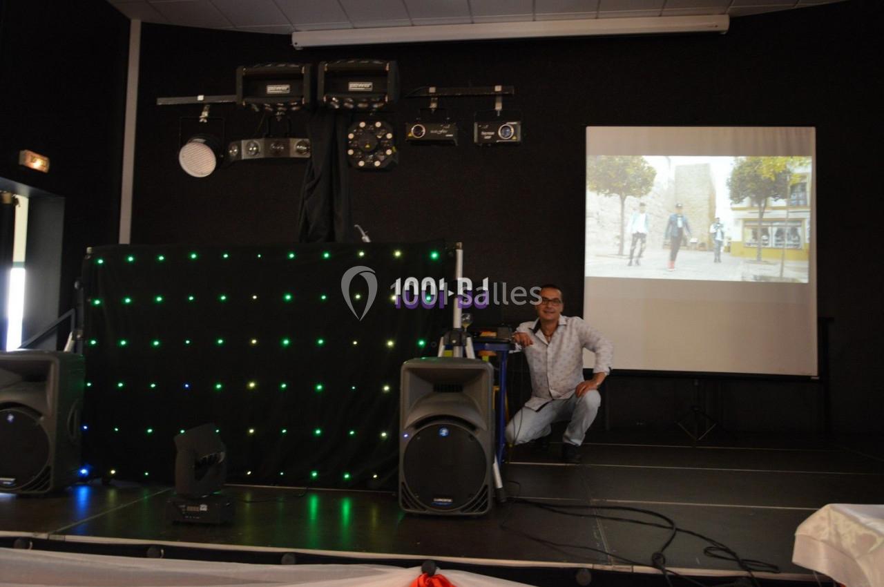Un homme accroupi près d'une table de mixage sur une scène équipée de lumières et d'un écran projetant une image.