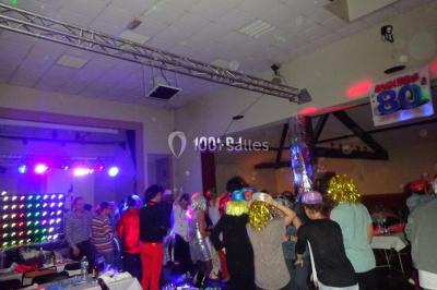 Un homme souriant se tient près d'une table de mixage éclairée, avec un écran projetant une vidéo en arrière-plan.