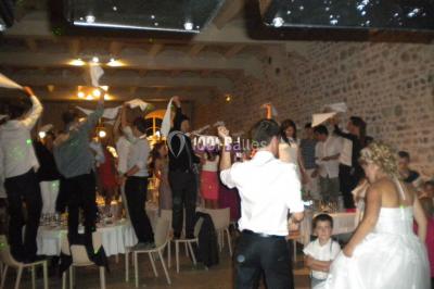 Un homme souriant se tient près d'une table de mixage éclairée, avec un écran projetant une vidéo en arrière-plan.