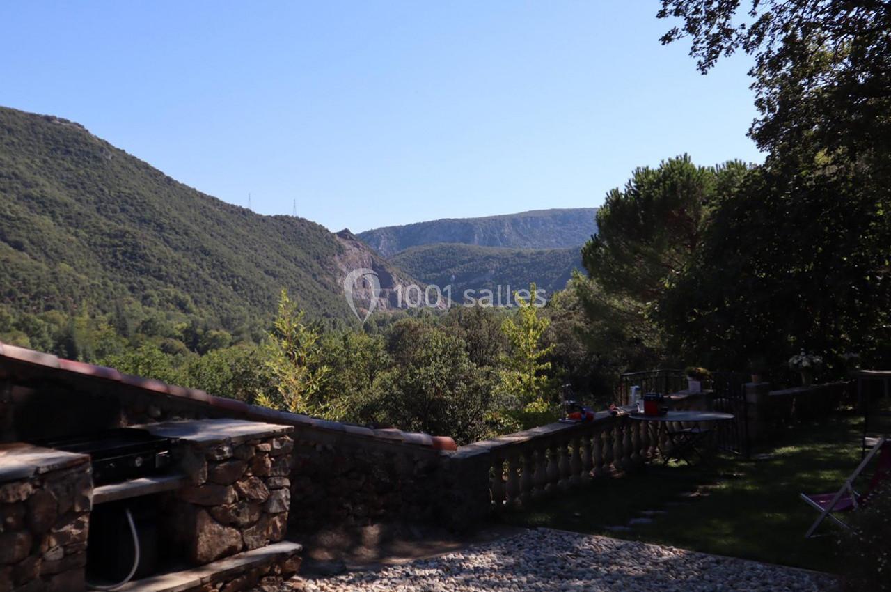 Vue sur un paysage vallonné avec des collines boisées, une terrasse en pierre et un espace extérieur ombragé.