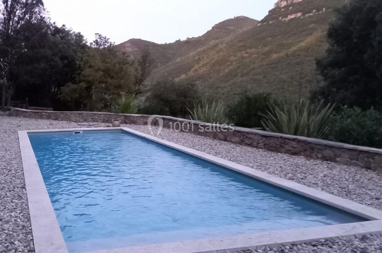 Piscine rectangulaire entourée de graviers, avec des collines verdoyantes en arrière-plan.