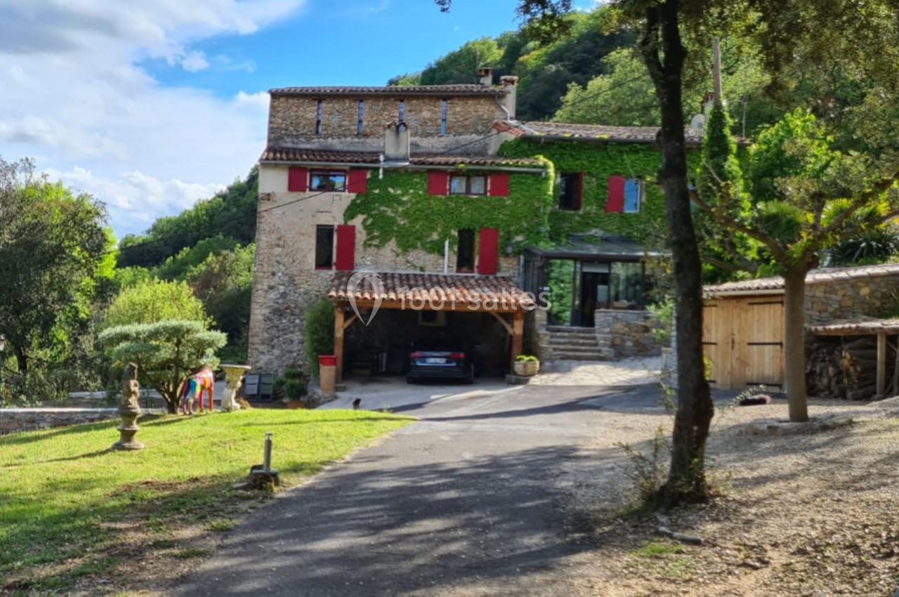 Maison en pierre avec volets rouges, entourée de verdure, une allée mène à un abri pour voiture et un jardin.