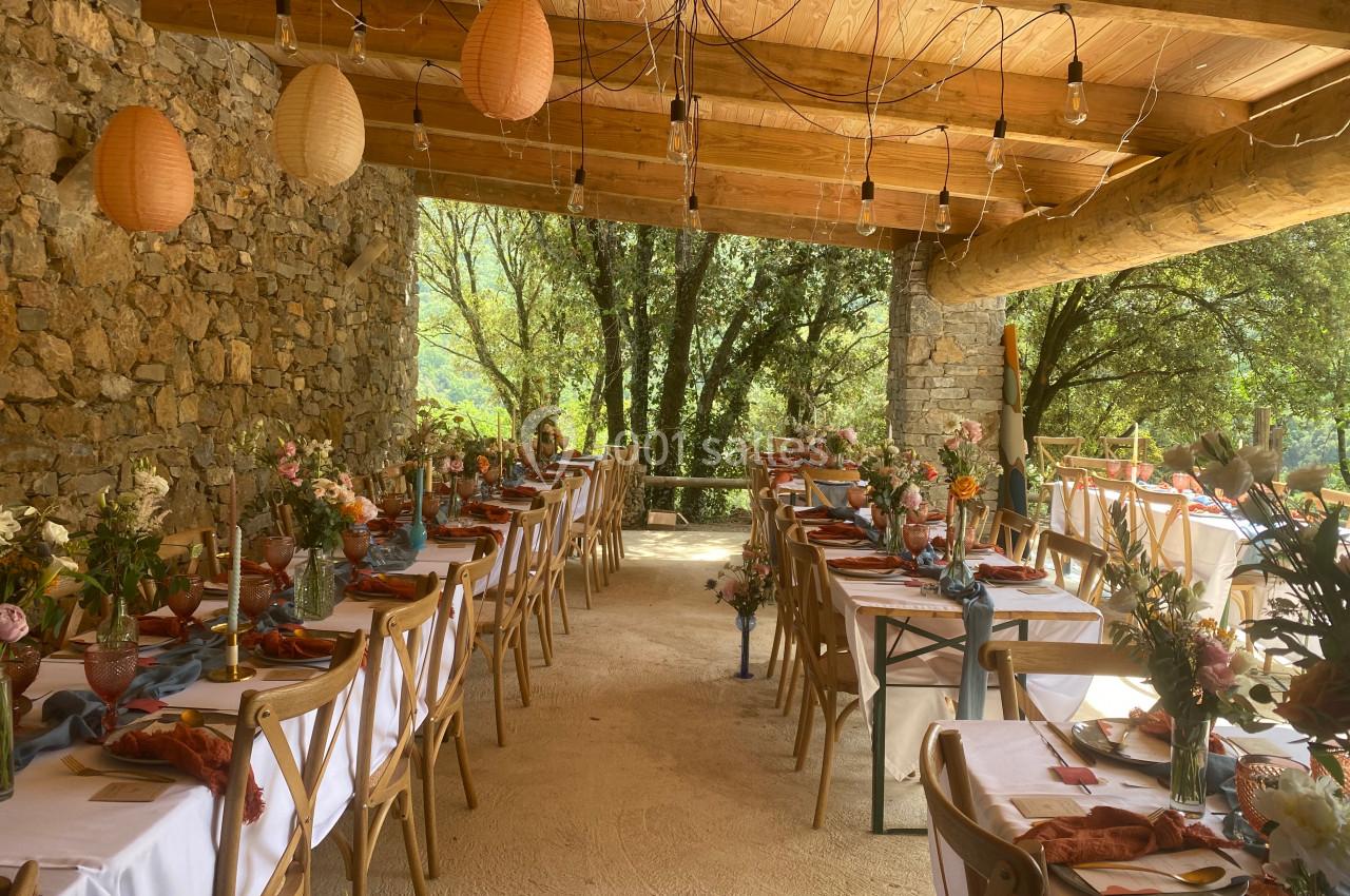 Salle de réception en plein air avec tables décorées de fleurs, nappes blanches et lanternes suspendues.