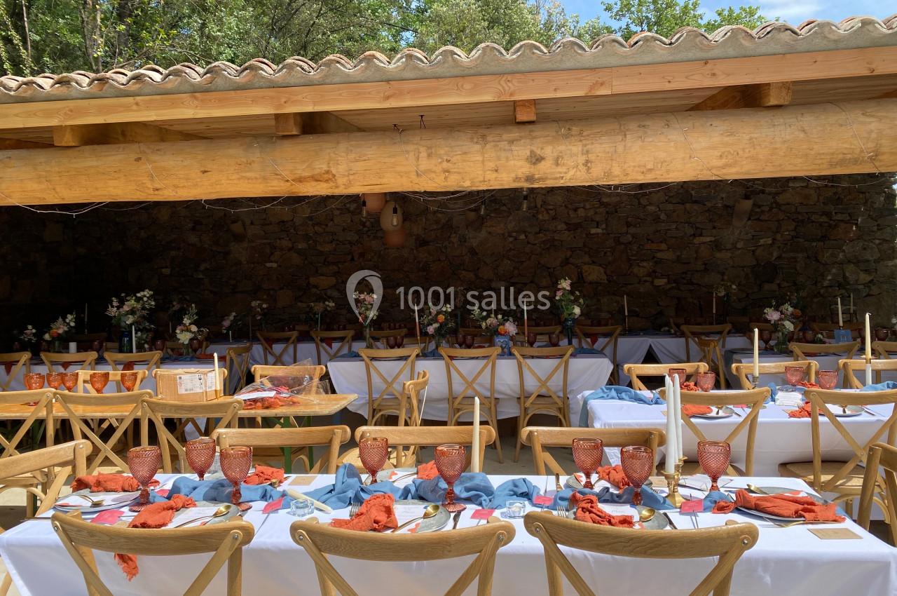 Tables décorées avec nappes blanches, serviettes colorées et vaisselle en terre cuite sous une pergola en bois.