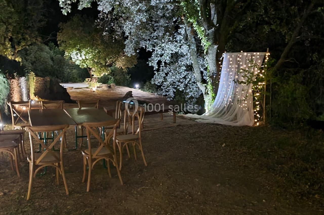 Espace extérieur nocturne avec table et chaises en bois, éclairage doux et décor lumineux sous des arbres.