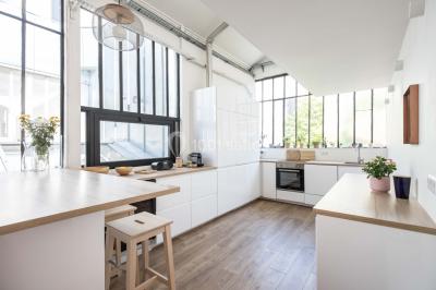 Salle de bain lumineuse avec baignoire blanche, mur rose, plante en pot et vue sur un escalier en bois.