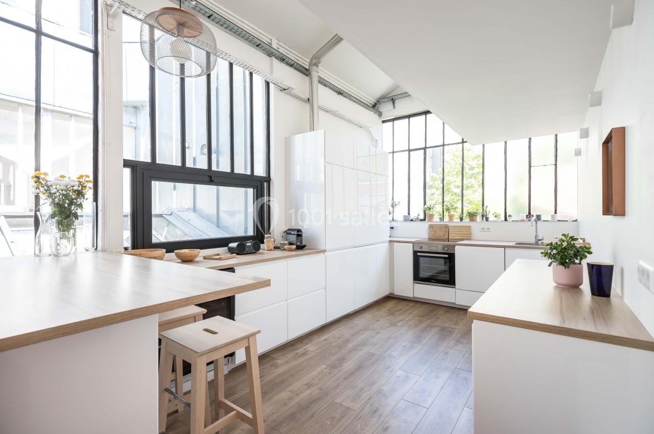 Cuisine lumineuse avec meubles blancs, plan de travail en bois, grandes fenêtres et sol en parquet clair.