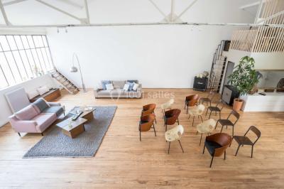 Salle de bain lumineuse avec baignoire blanche, mur rose, plante en pot et vue sur un escalier en bois.