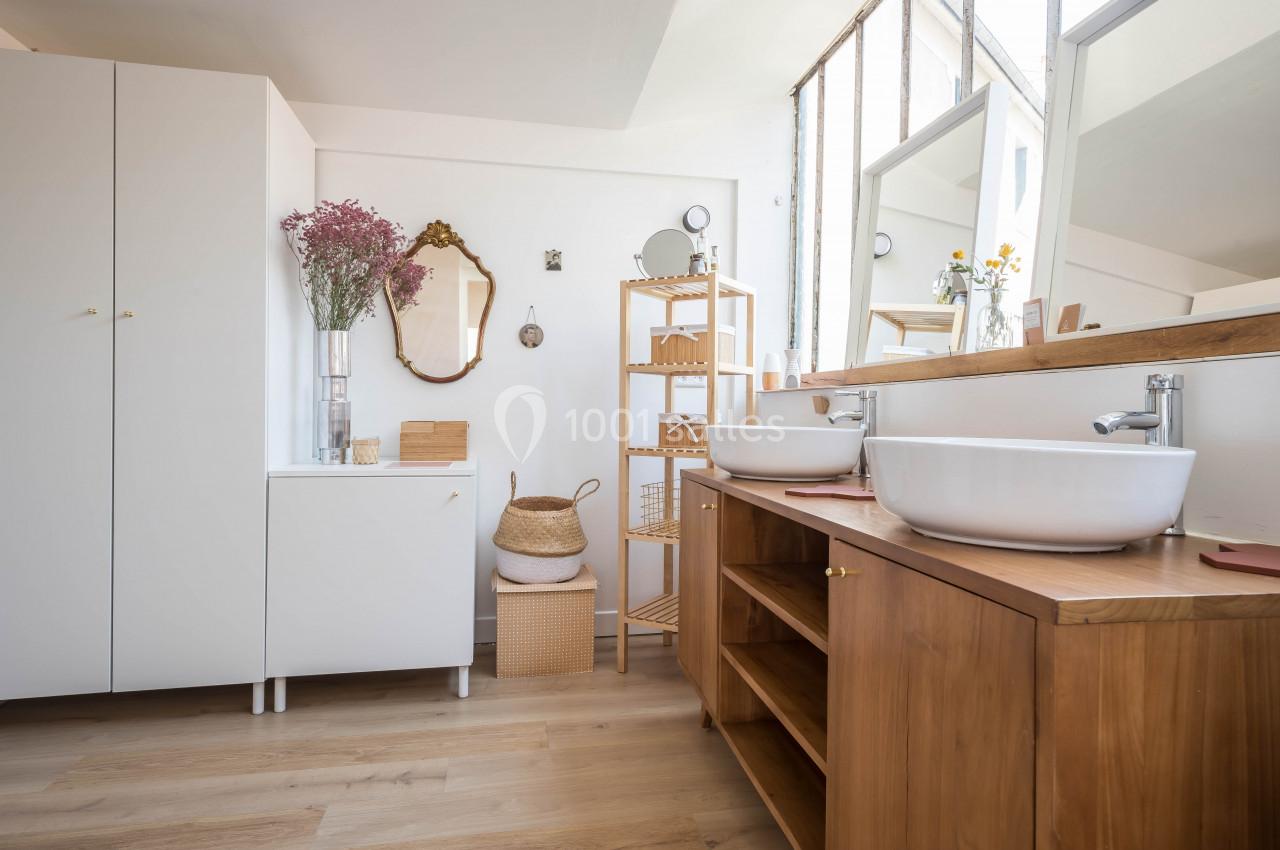Salle de bain lumineuse avec meubles en bois, vasques blanches, miroirs et décoration minimaliste.