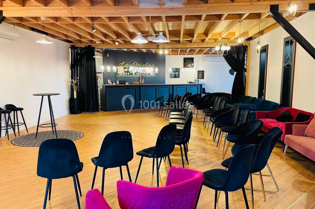 Salle lumineuse avec parquet, chaises disposées en rangées, bar au fond et plafond en bois apparent.