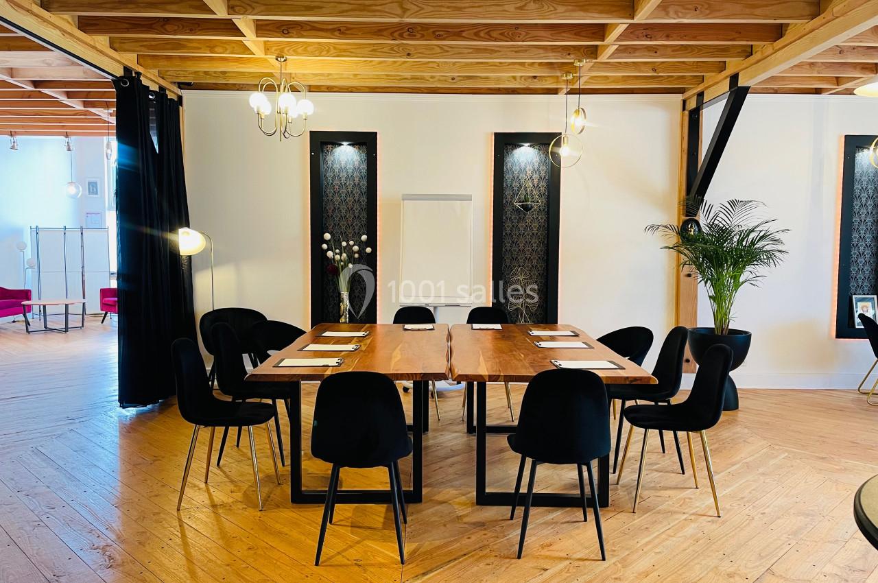 Salle de réunion lumineuse avec une grande table en bois entourée de chaises noires, éclairée par des suspensions.