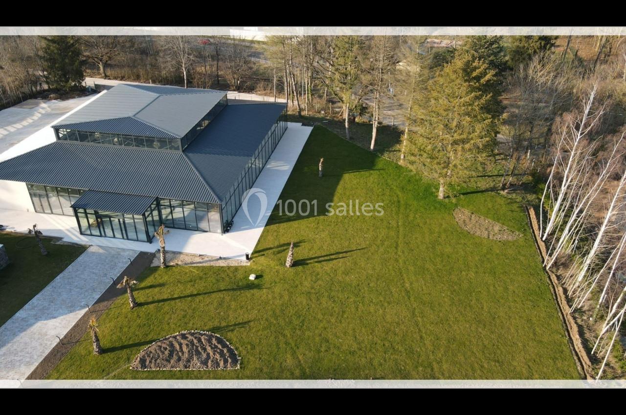 Vue aérienne d'un bâtiment moderne avec toit en métal entouré d'une pelouse et d'arbres en bordure.