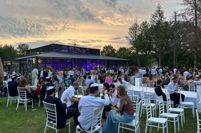 Un groupe de personnes en tenue traditionnelle célèbre un événement sous des lustres dans une grande salle éclairée.