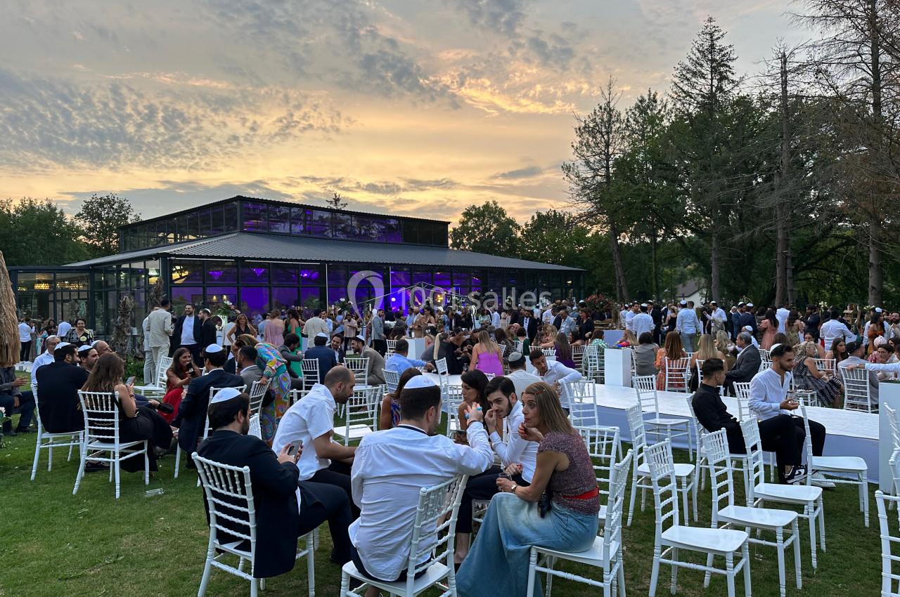 Groupe de personnes assises et debout dans un jardin, près d'une salle vitrée, au coucher du soleil.