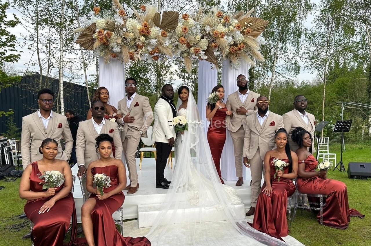 Un couple de mariés entouré de leurs demoiselles et garçons d'honneur en tenue élégante, devant une arche fleurie.