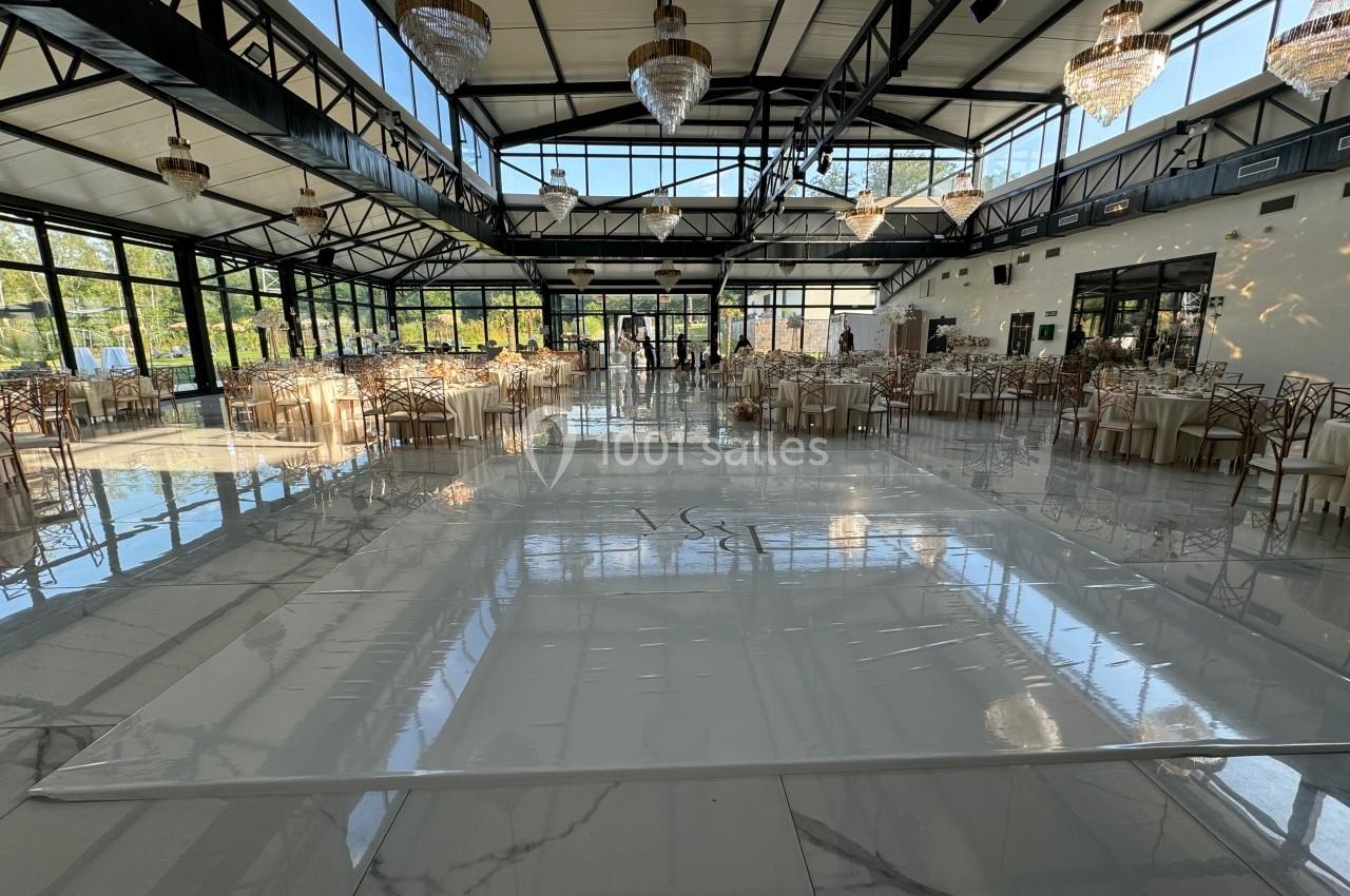 Salle de réception spacieuse avec tables dressées, grandes baies vitrées et lustres suspendus au plafond.