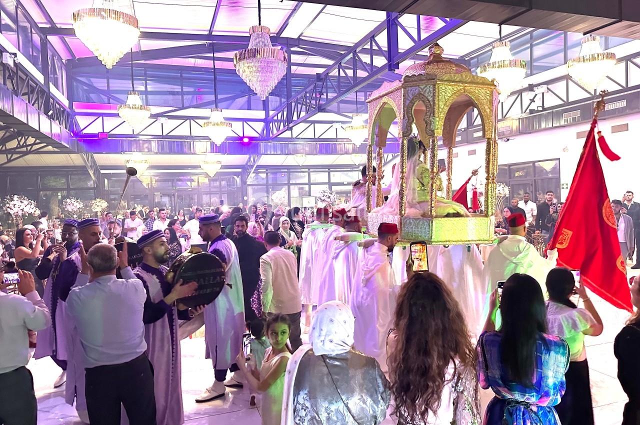 Un groupe de personnes en tenue traditionnelle célèbre un événement sous des lustres dans une grande salle éclairée.