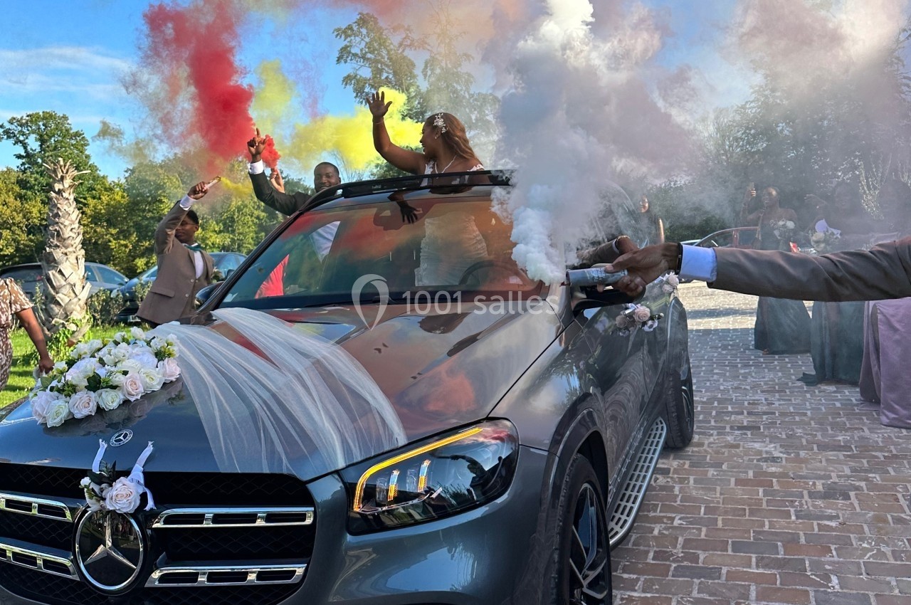 Voiture décorée pour un mariage avec des invités tenant des fumigènes colorés, célébrant dans une ambiance festive.