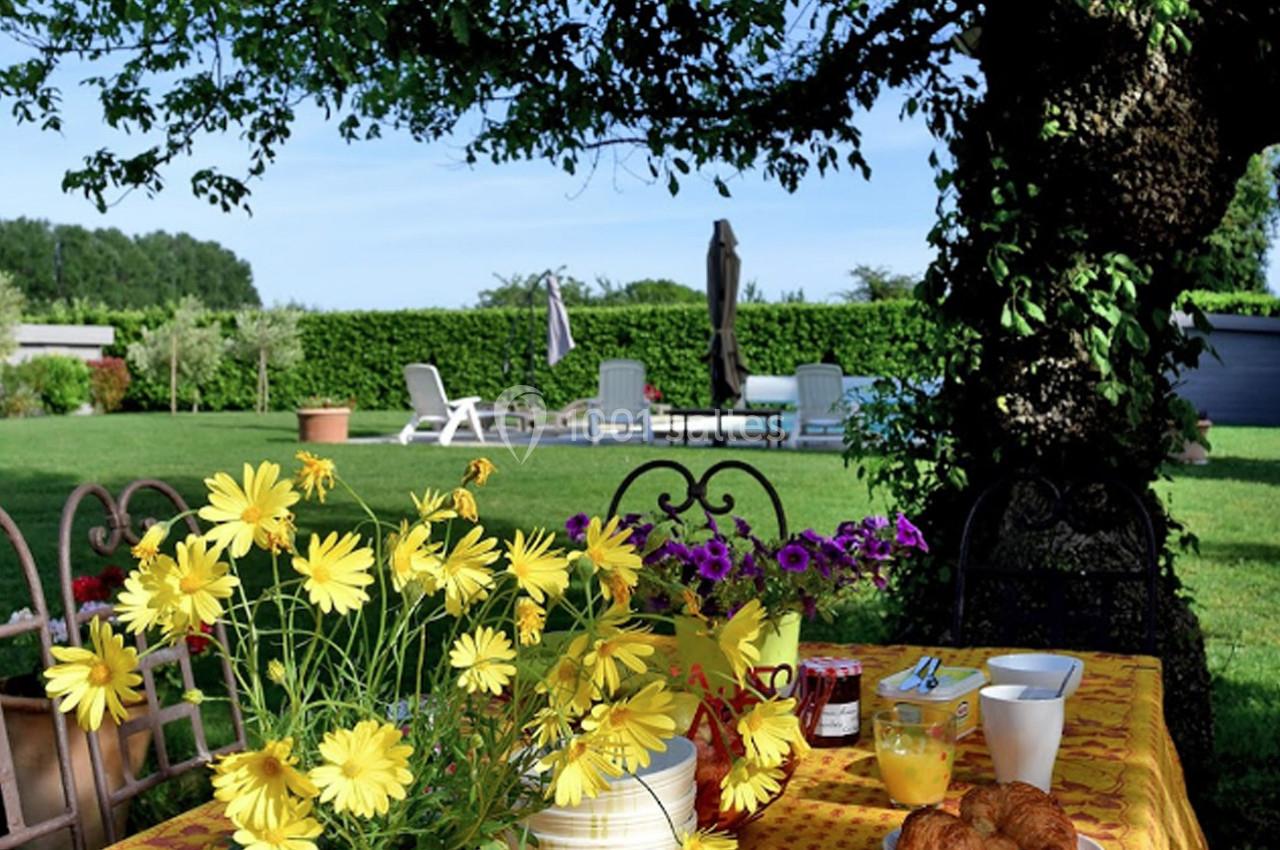 Table de petit-déjeuner avec fleurs jaunes, croissants et jus d'orange, dans un jardin verdoyant avec piscine en arrière…
