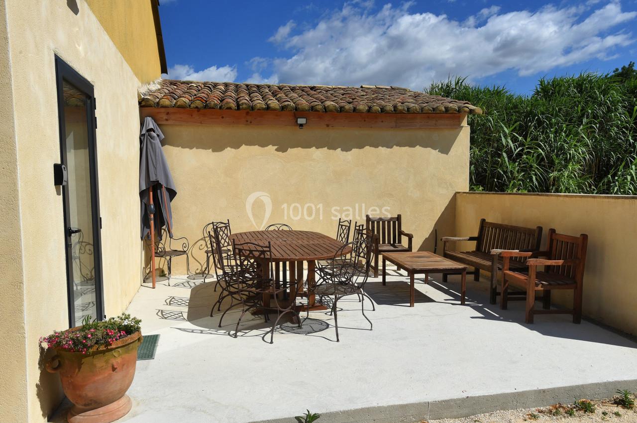 Terrasse ensoleillée avec mobilier de jardin en bois et métal, adossée à un mur beige sous un ciel bleu.