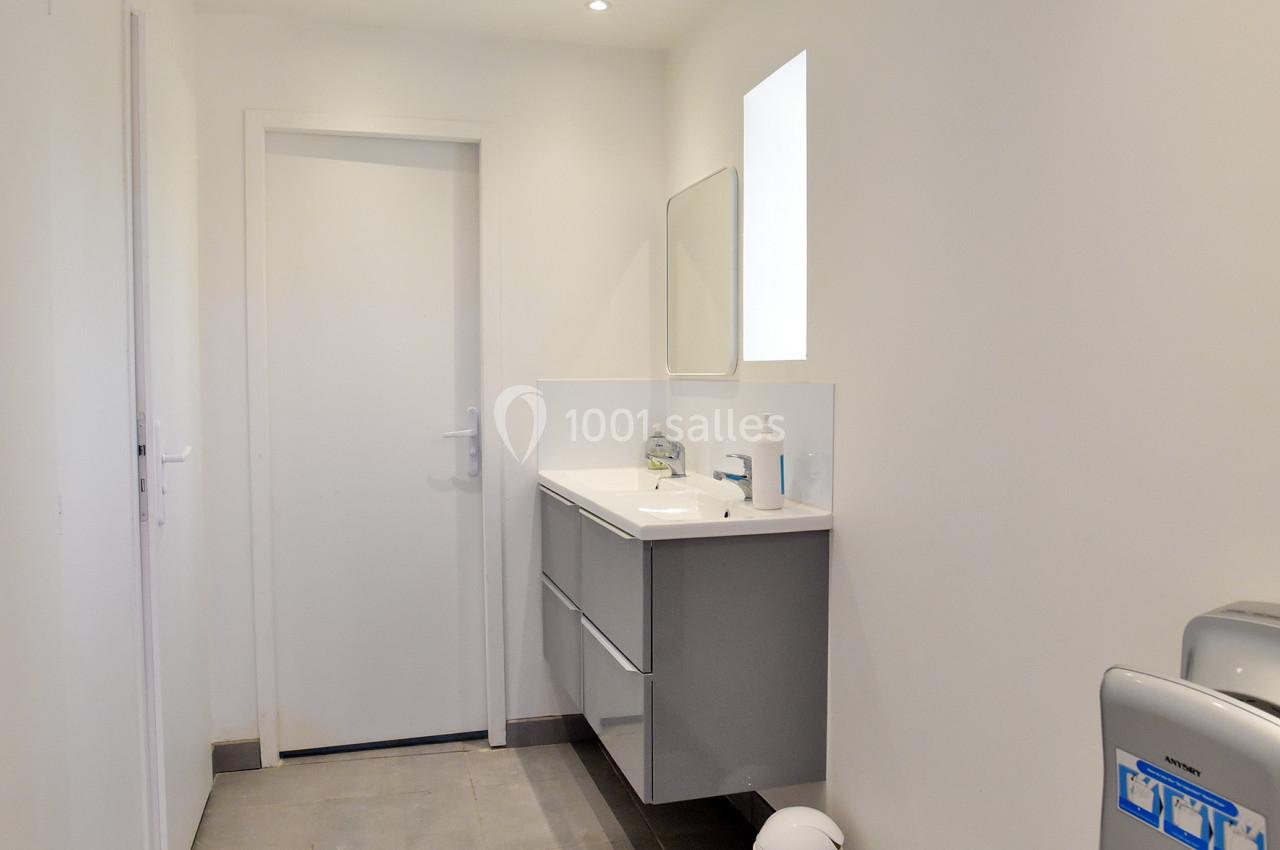 Salle de bain moderne avec carrelage gris, meuble suspendu, miroir, poubelle blanche et éclairage encastré.