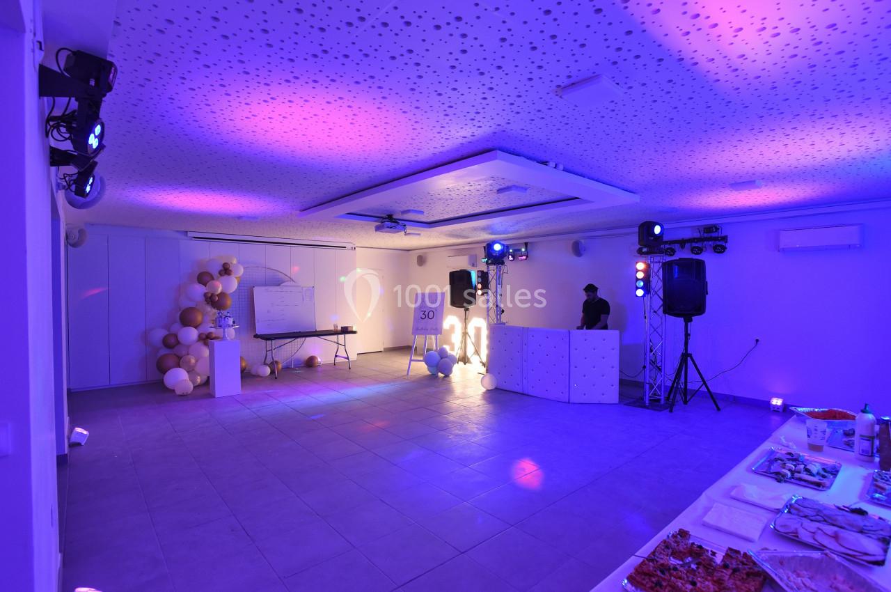 Salle décorée pour un événement avec éclairage violet, table de buffet, ballons et espace DJ équipé.