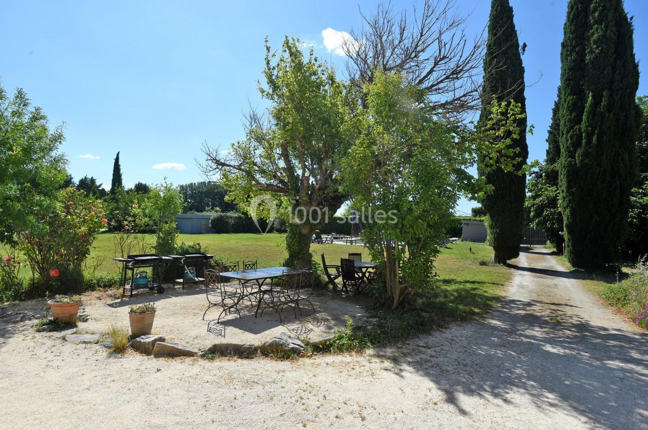 Terrasse extérieure avec table et chaises sous un arbre, entourée de verdure et de grands cyprès.