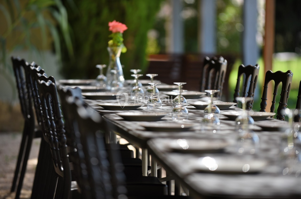Table dressée en extérieur avec des verres retournés, des assiettes et un vase contenant une fleur orange.