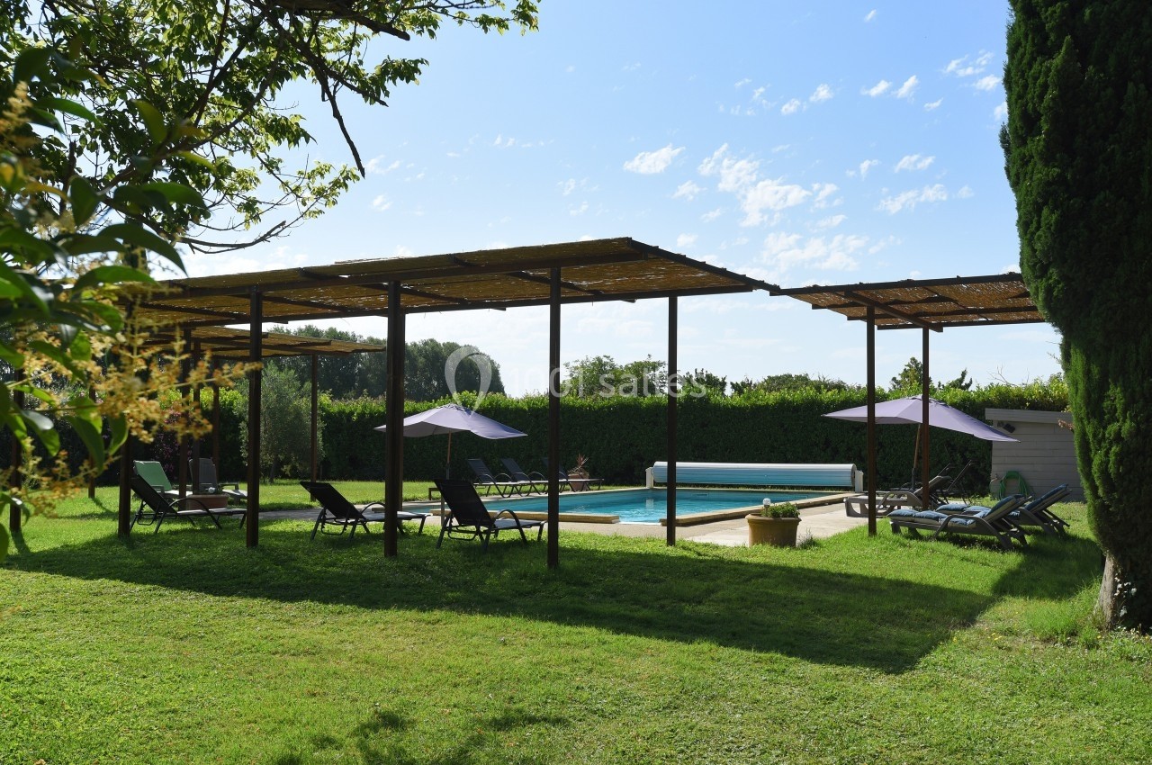 Espace extérieur avec piscine, chaises longues et pergolas ombragées, entouré de verdure et d'arbres.