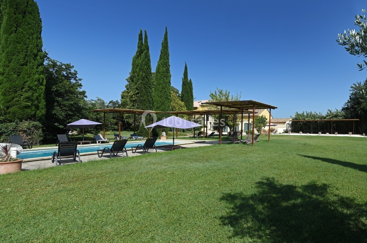 Jardin avec piscine, transats sous des parasols, pelouse bien entretenue et arbres en arrière-plan.