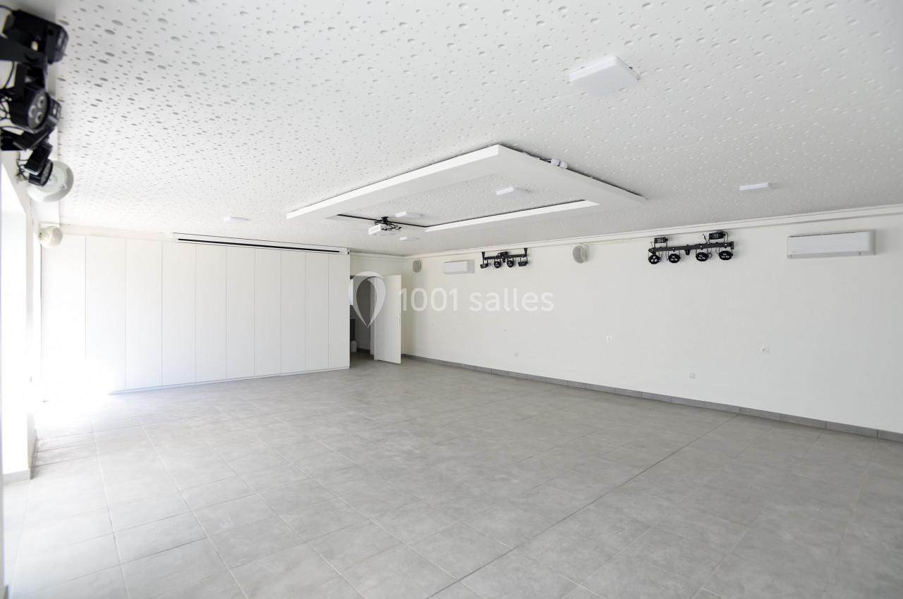 Salle vide avec carrelage gris, murs blancs, plafond équipé de luminaires et matériel audiovisuel.