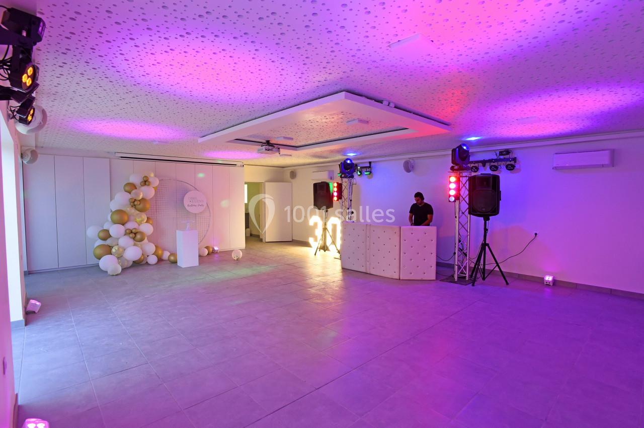Salle de réception décorée avec des ballons, un DJ en arrière-plan et un éclairage coloré.