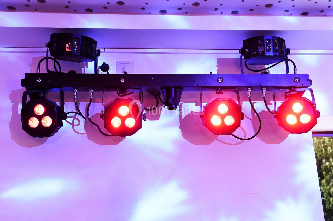 Projecteurs LED rouges fixés sur une barre métallique, éclairant un mur avec des reflets lumineux violets.