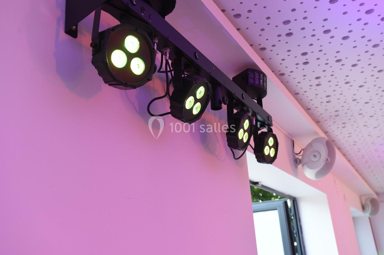 Projecteurs LED suspendus émettant une lumière colorée dans une pièce avec un plafond perforé.