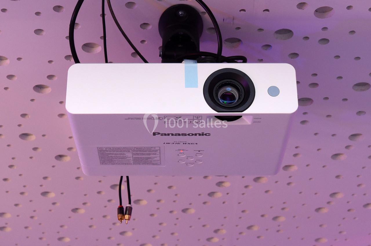 Projecteur blanc fixé au plafond perforé, câbles audio visibles en dessous.