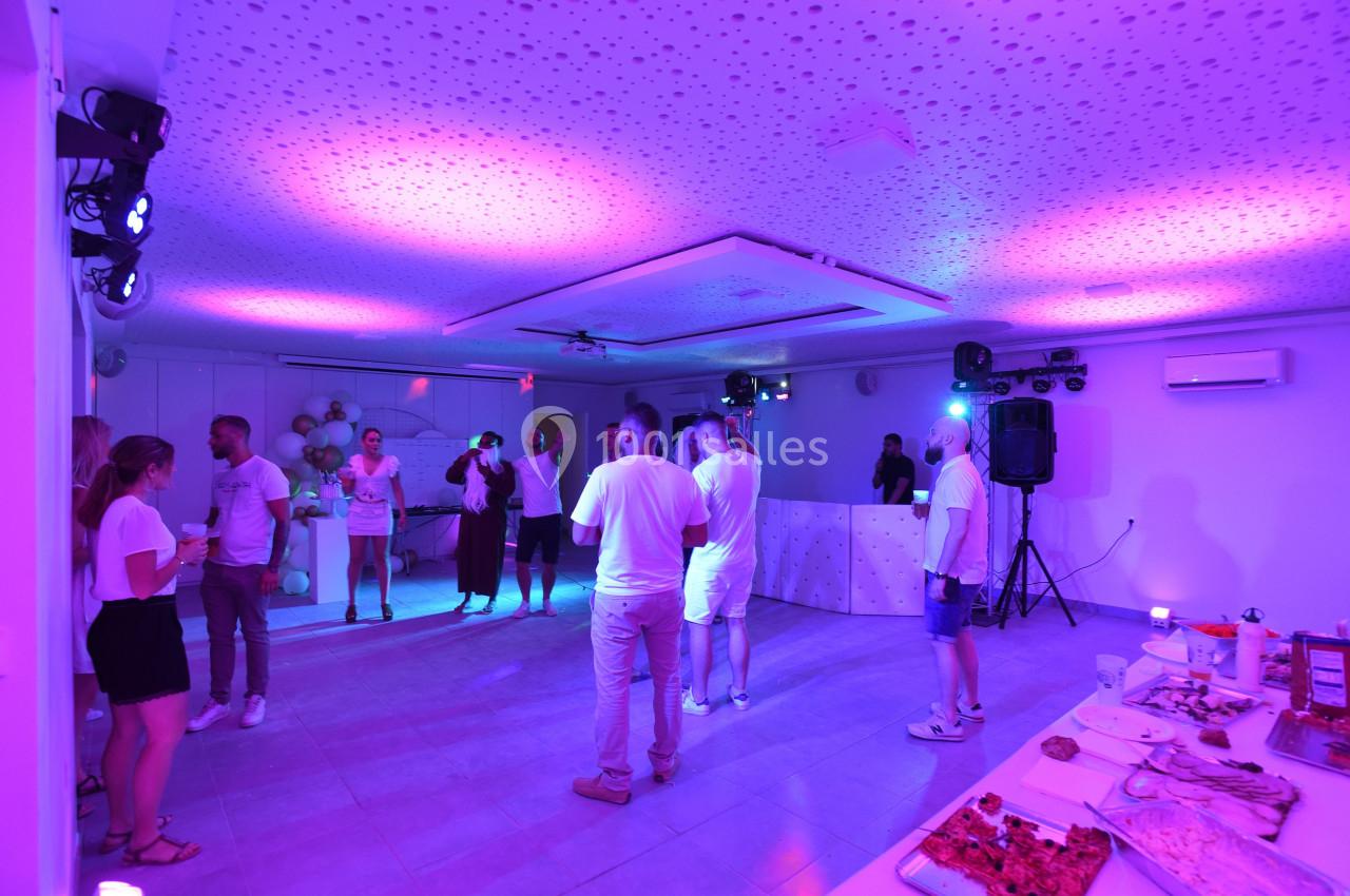 Des personnes discutent et dansent dans une salle éclairée par des lumières colorées, avec un buffet au premier plan.