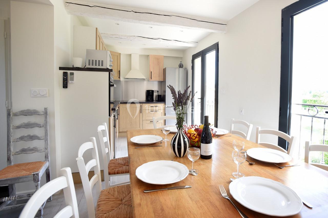 Salle à manger lumineuse avec une grande table en bois dressée, cuisine ouverte en arrière-plan.
