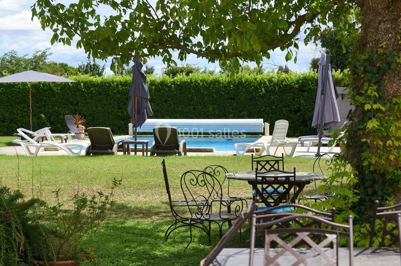 Chaises longues et parasols disposés autour d'une piscine extérieure, entourée de verdure et d'arbres.