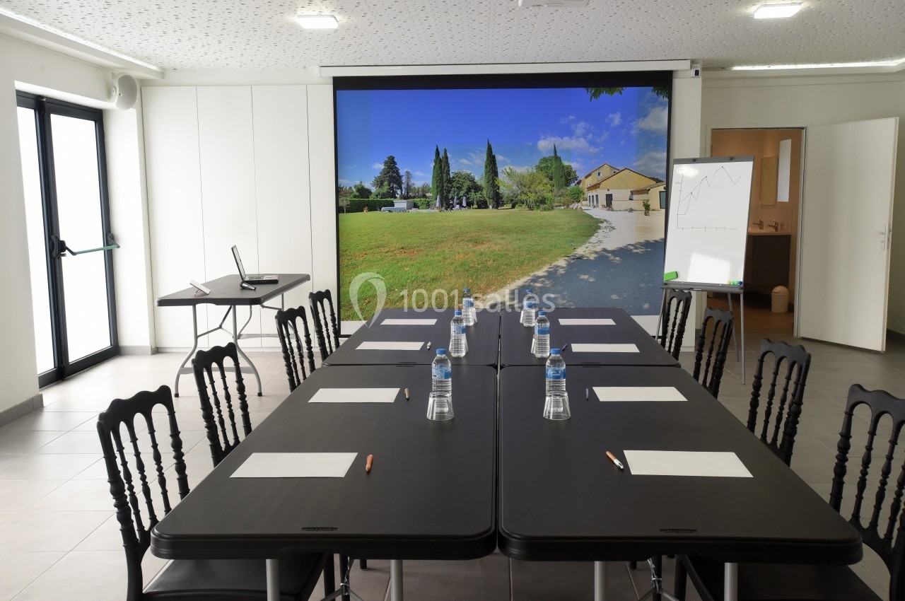 Salle de réunion lumineuse avec une grande table, des chaises, des bouteilles d'eau, un tableau blanc et un écran affichant…