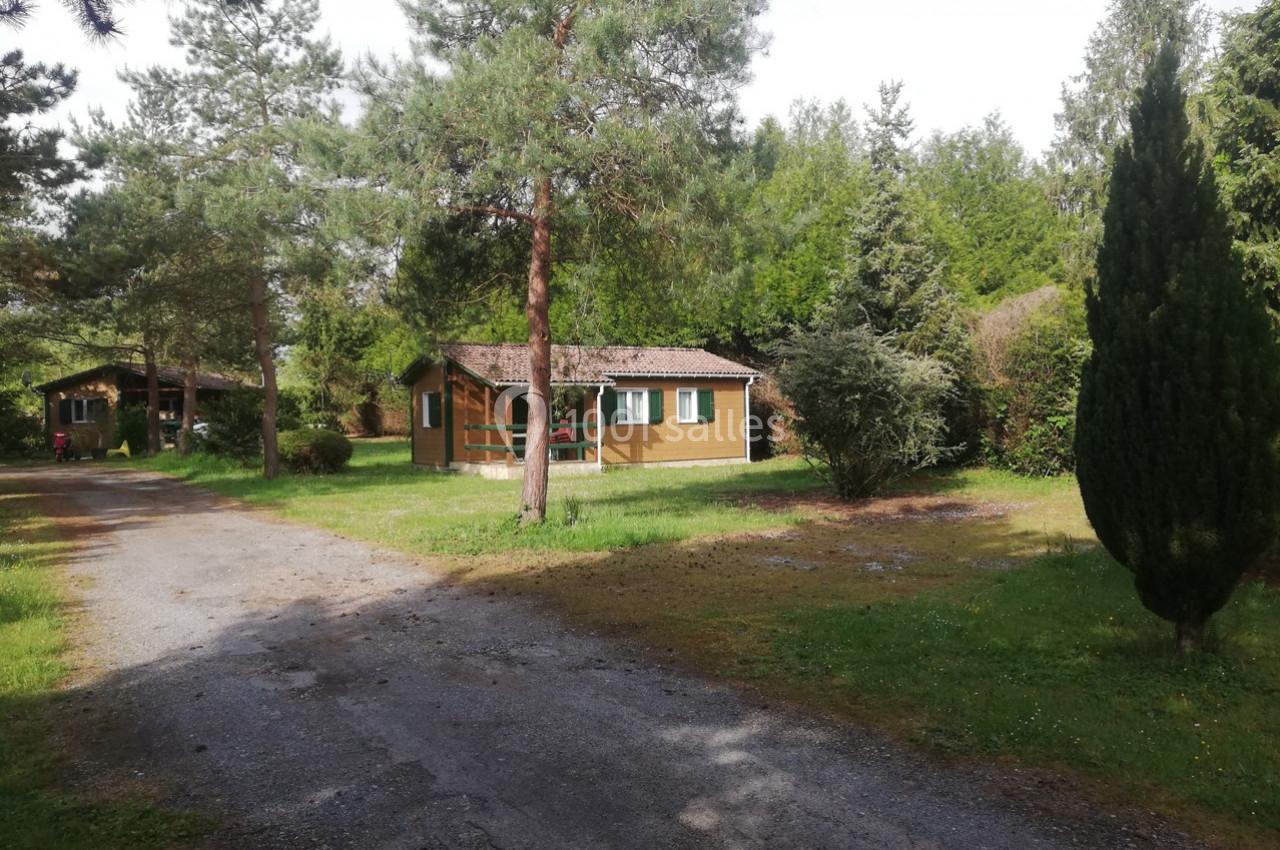 Chalet en bois entouré de verdure avec un chemin en gravier au premier plan et des arbres en arrière-plan.
